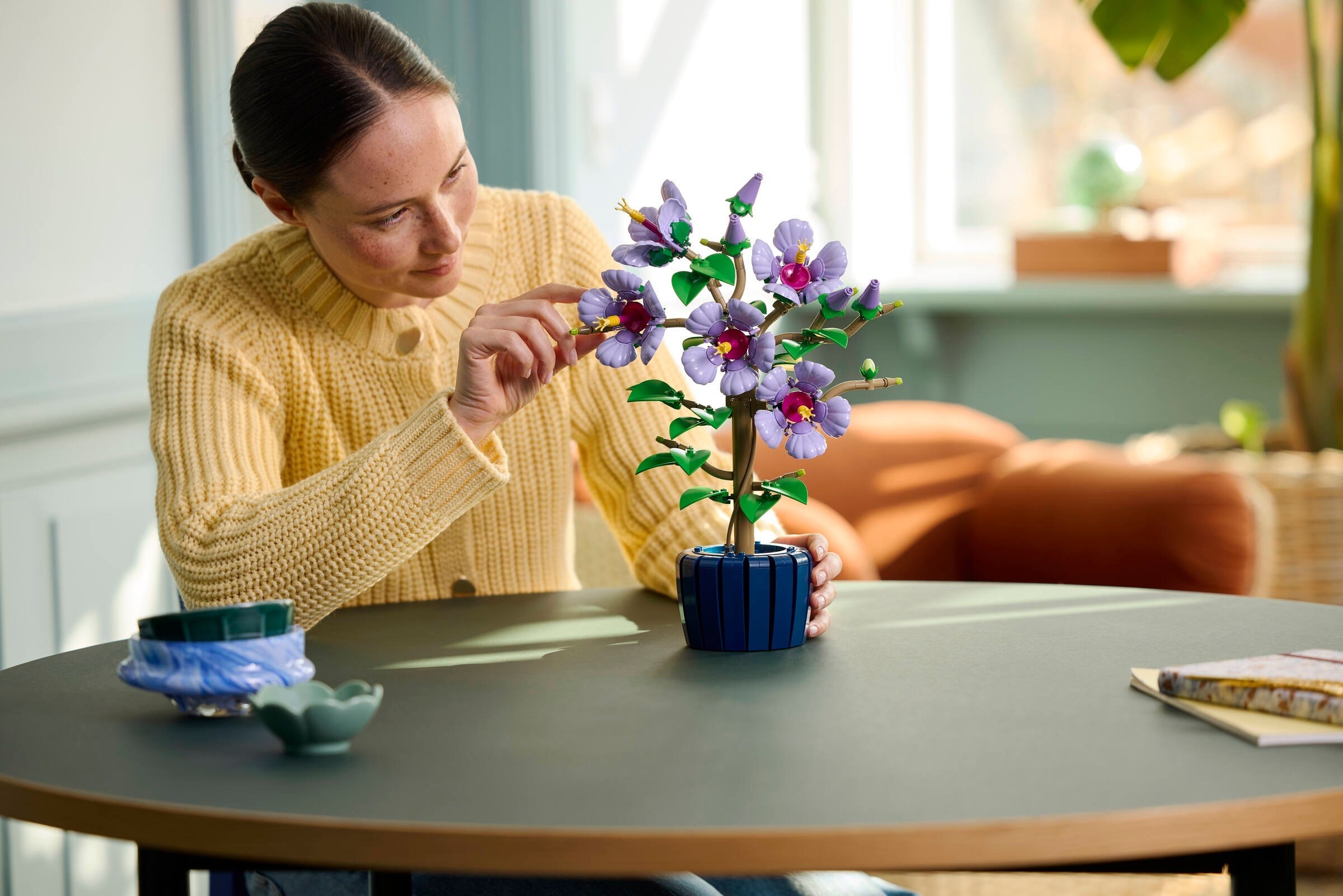 Interactive scene showing LEGO 10372 Hibiscus being adjusted and customized by builder in home setting